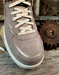 Brown suede sneaker with off-white laces on a rustic wooden surface with gears in the background