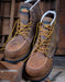 Pair of brown work boots with yellow laces on a wooden background