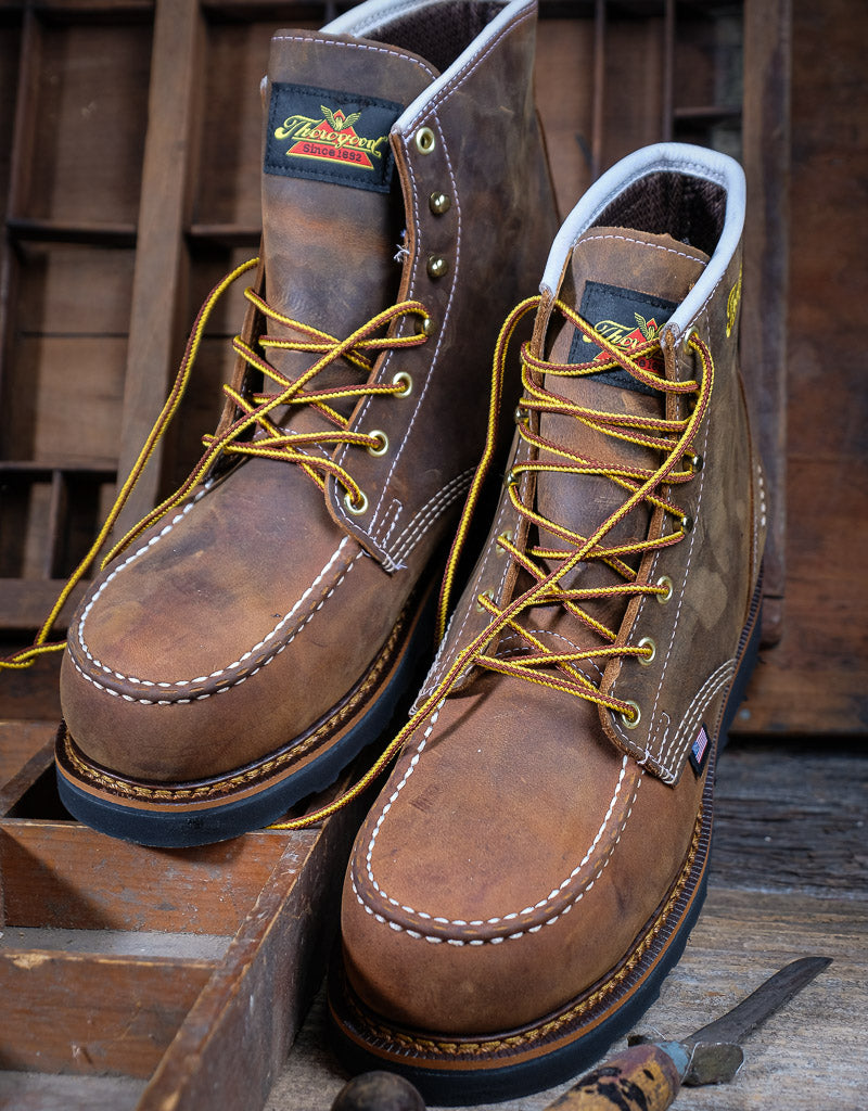 Pair of brown work boots with yellow laces on a wooden background