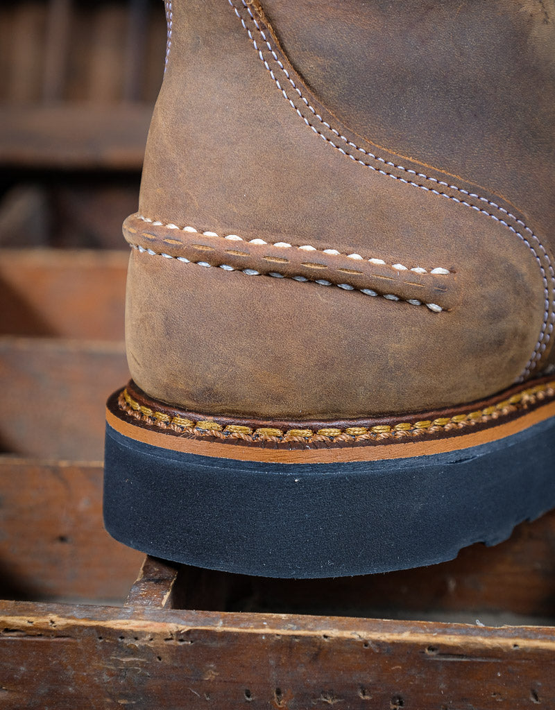 Close-up of a brown leather boot heel with visible stitching on a wooden surface.