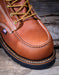 Brown leather boot with yellow laces on a wooden surface