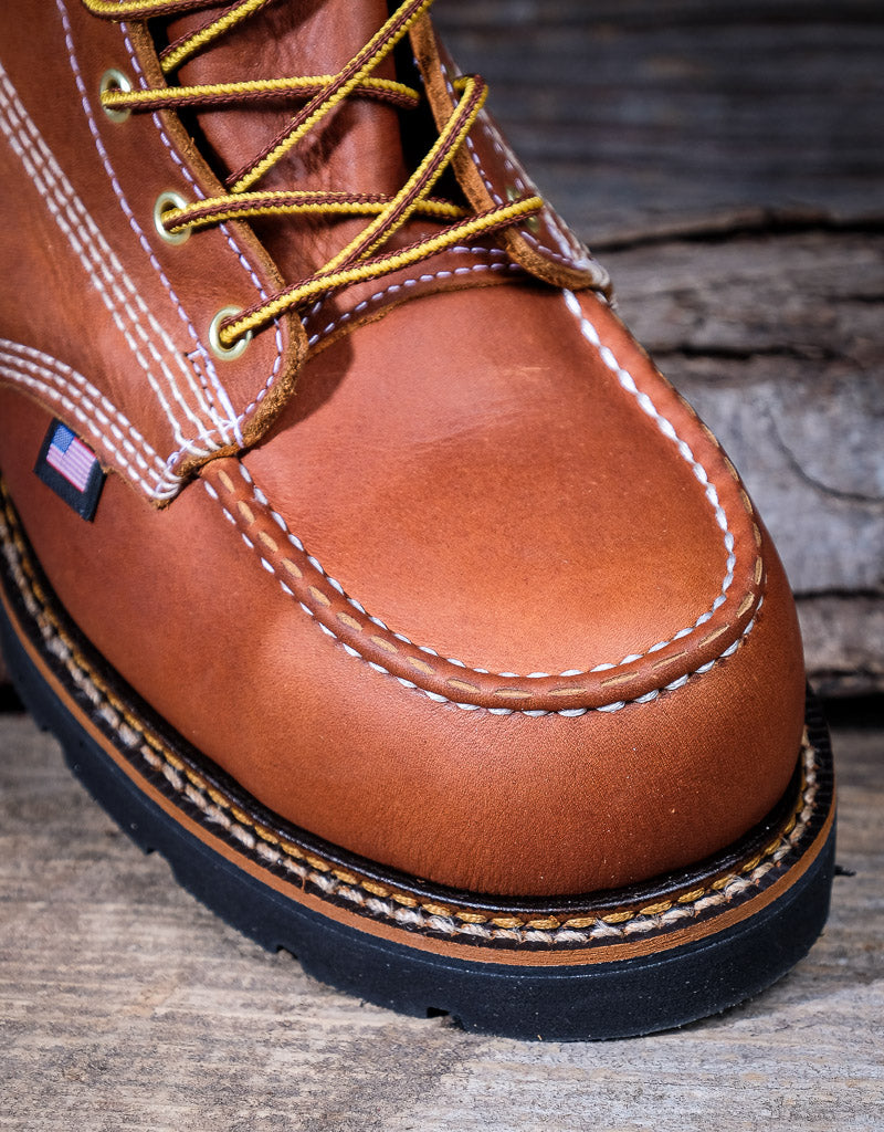 Brown leather boot with yellow laces on a wooden surface