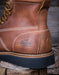 Close-up of a brown leather boot with visible stitching and brand logo on a wooden surface.