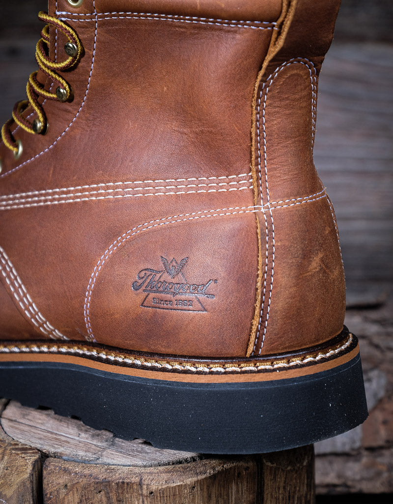 Close-up of a brown leather boot with visible stitching and brand logo on a wooden surface.