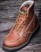 Brown leather boot with gold laces on a wooden surface