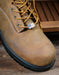 Brown leather boot with yellow laces on a wooden surface