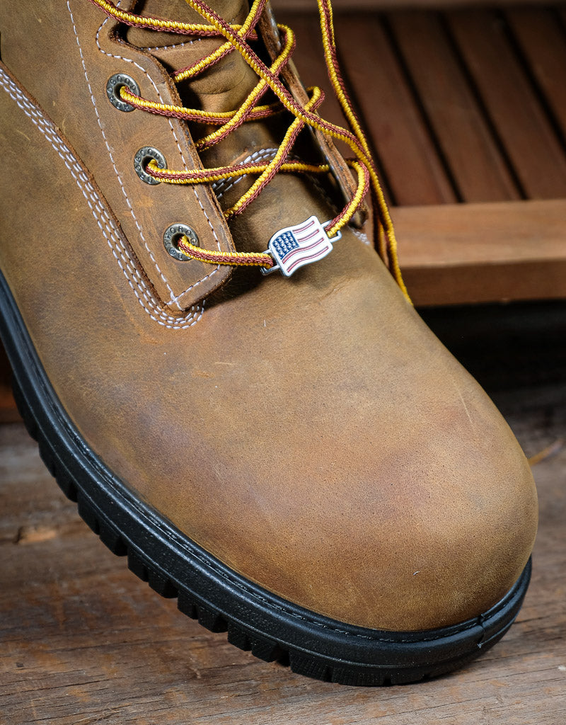 Brown leather boot with yellow laces on a wooden surface