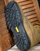 Brown work boot with black sole on a wooden floor