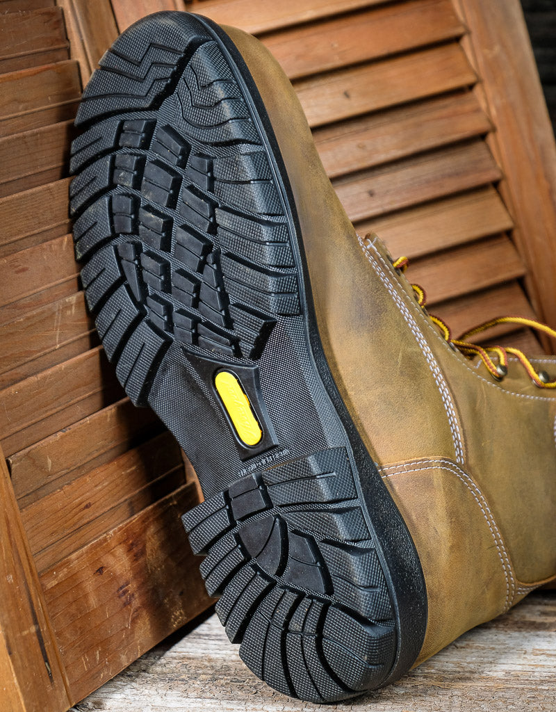 Brown work boot with black sole on a wooden floor