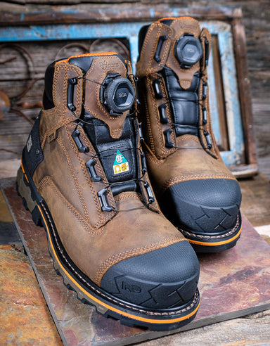 Pair of brown work boots with black soles on a rustic wooden surface
