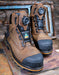 Pair of brown work boots with black soles on a rustic wooden surface