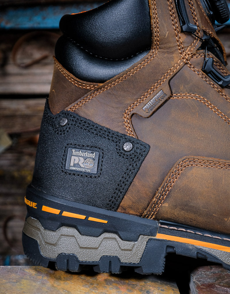 Close-up of a brown leather boot with a label that says 'Waterproof' and 'Timberland PRO composite toe' on a wooden surface.
