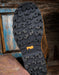 Close-up of a brown leather shoe sole with rugged tread pattern on a wooden surface