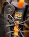 Close-up of a Timberland high-top work boot in  black with bright orange accents, including the tongue pull tab, lace loop, and branding patch.