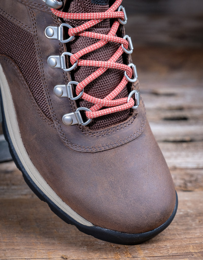 Brown hiking boot with pink laces on a wooden surface