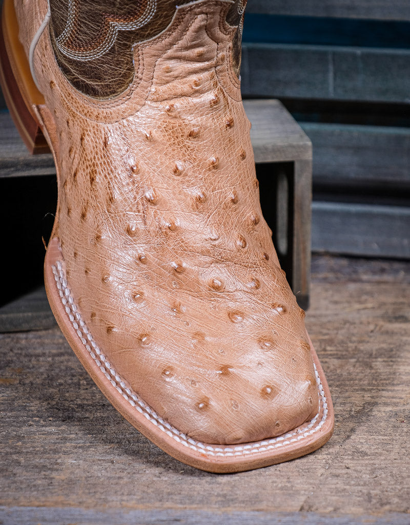 Close-up of a tan ostrich leather boot with detailed stitching on a wooden surface.