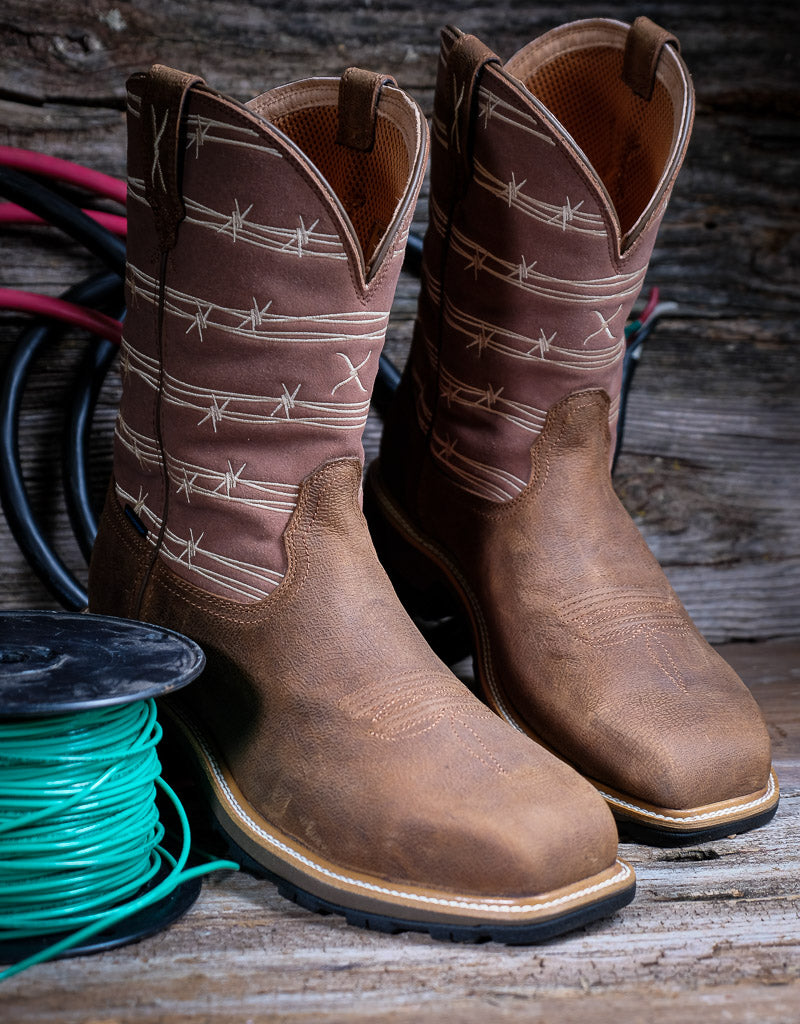 Pair of brown cowboy boots with barbed wire design on a wooden surface with a spool of green thread.