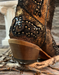 Close-up of a cowboy boot heel with intricate stitching and studs on a wooden surface.
