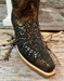 Close-up of a cowgirl boot snip toe with metallic studs on a wooden surface.
