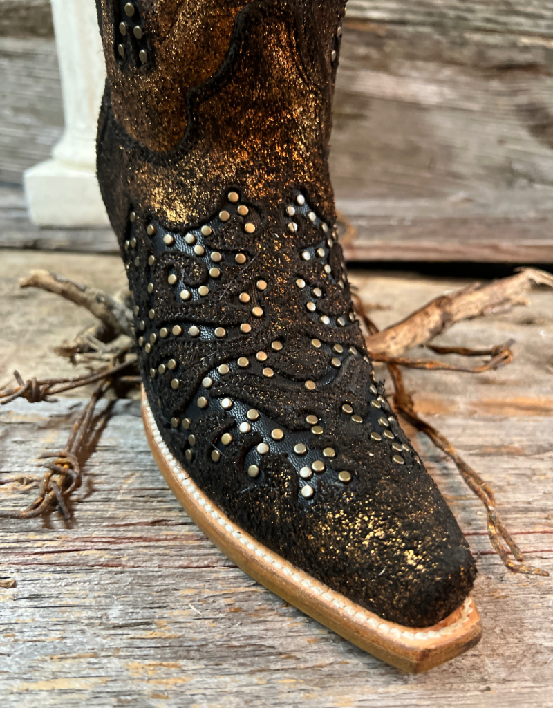 Close-up of a cowgirl boot snip toe with metallic studs on a wooden surface.