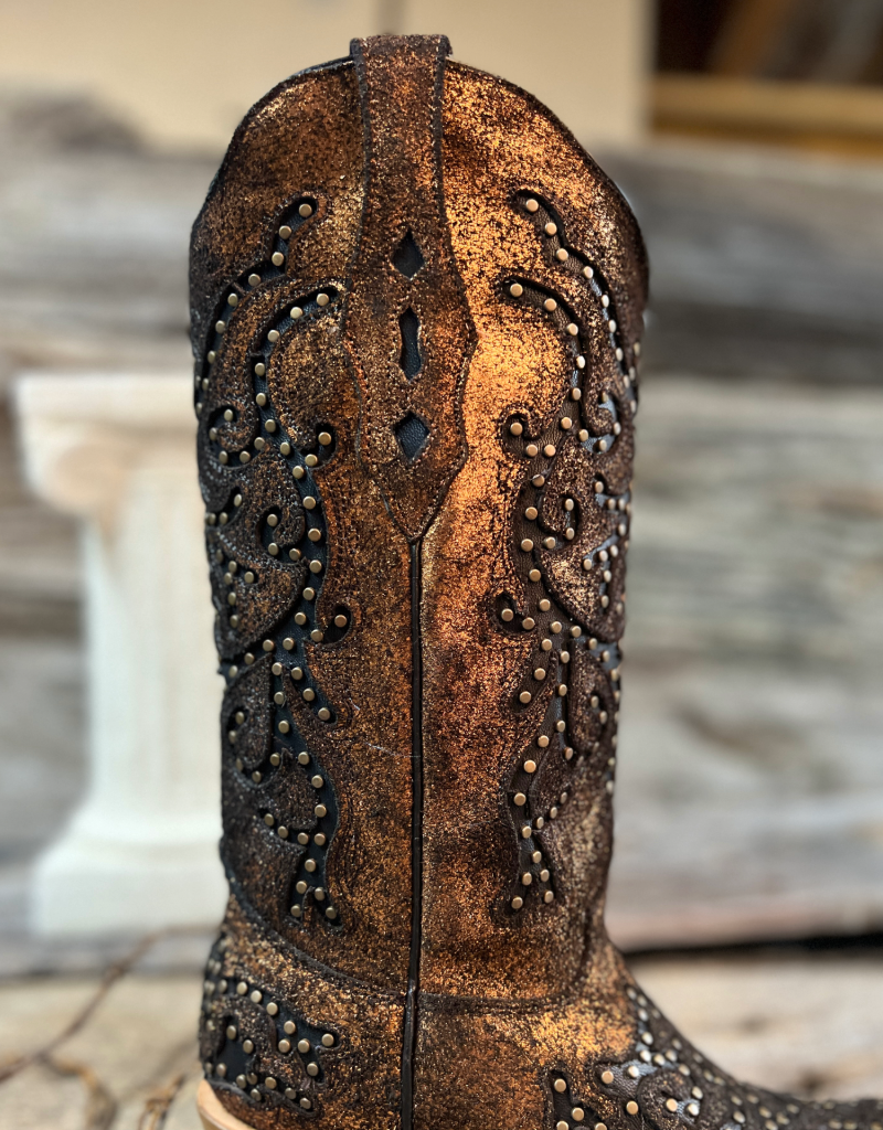 Close-up of a cowgirl boot shaft with intricate studded detailing and black embroidery on a blurred background.