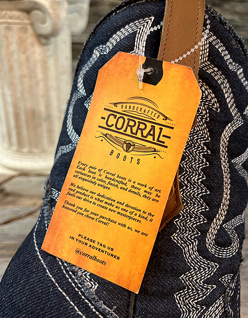 An orange tag attached to a pair of blue boots reading " Handcrafted Corral Boots. Every pair of Corral Boots is a work of art. Each boot is handcrafted, there may be variances in color, finish, and details, they are all exquisitely unique. We believe our dedication and devotion to the end product is what make us one of a kind, it fuels our drive to create new masterpieces. Thank you for your purchase with us we are honored you chose corral."