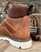 Brown leather boot, close up on heel area with padded collar and pull loop with a white sole on a rustic wooden background
