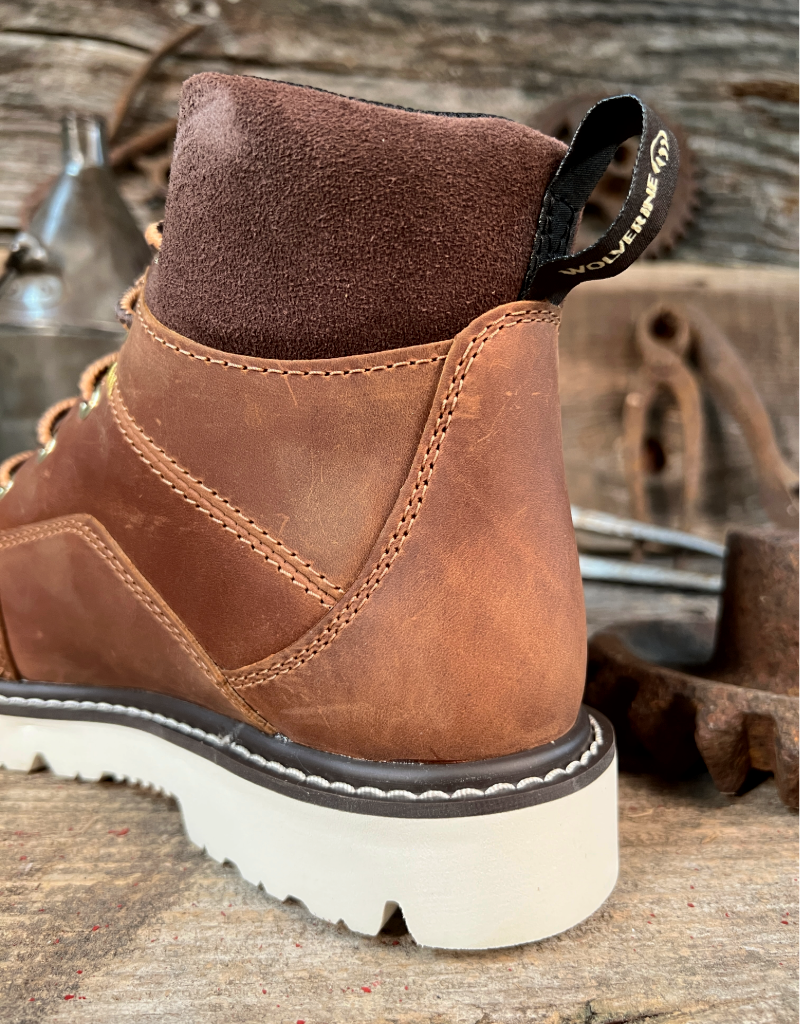 Brown leather boot, close up on heel area with padded collar and pull loop with a white sole on a rustic wooden background