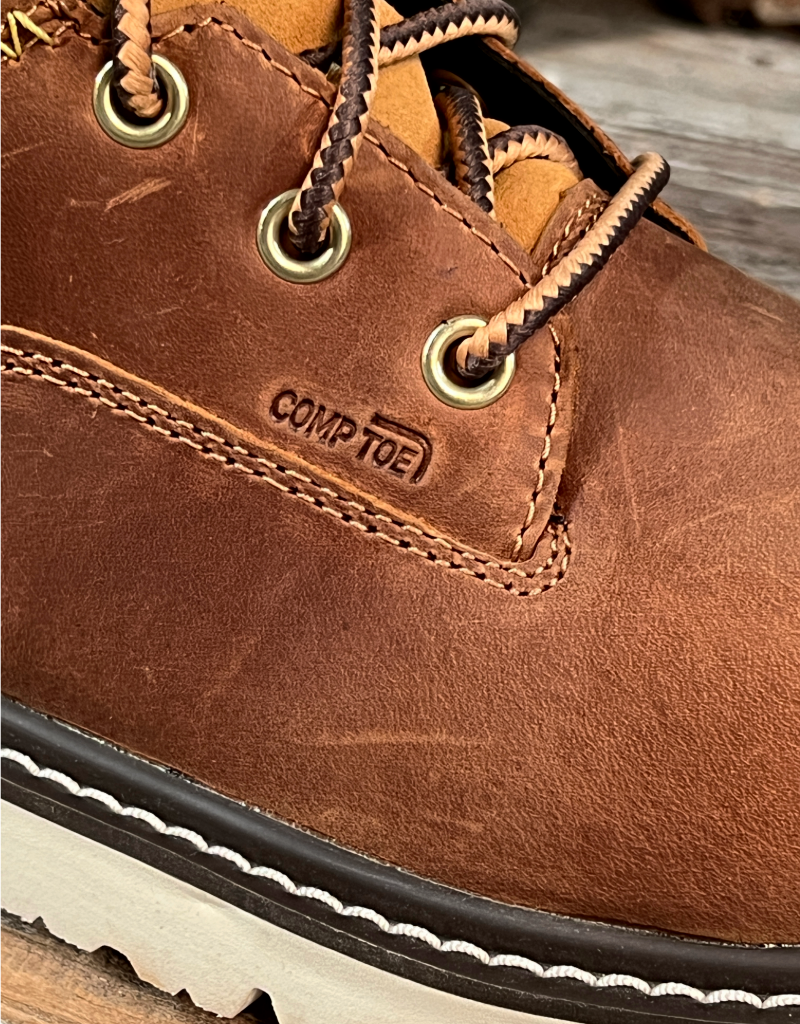 Close-up of a brown leather boot with 'Comp Toe' label on a wooden floor.