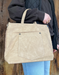 Beige handbag held by a person against a wooden background