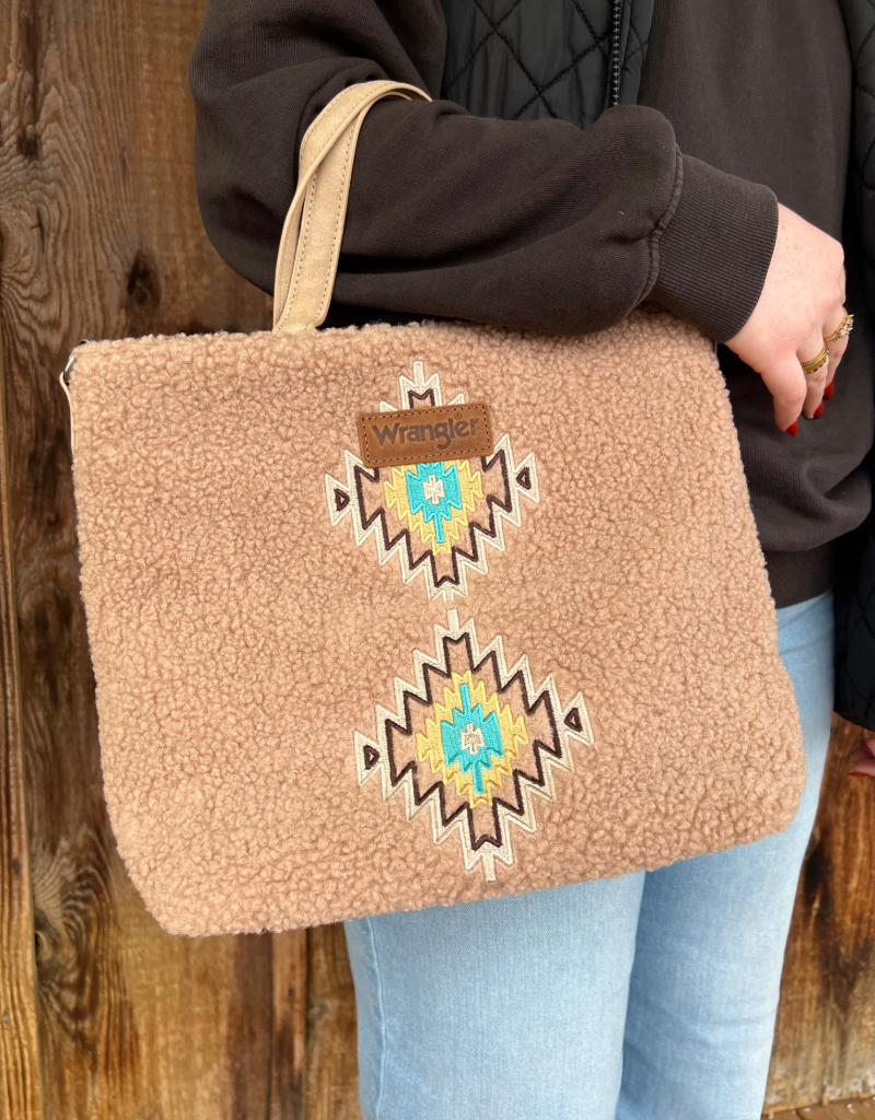 Person holding a tan sherpa bag with aztec decorative patterns and a visible Wrangler brand logo.