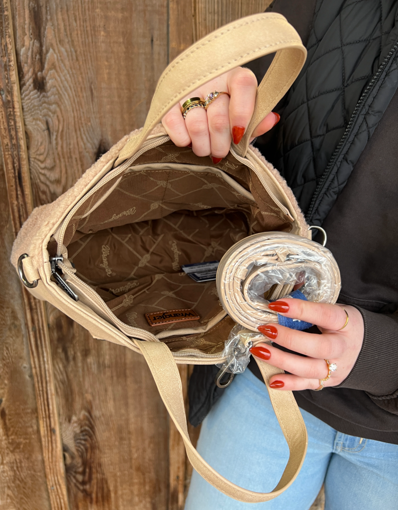 Person holding a beige handbag and crossbody strap with a wooden background