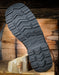 Close-up of a black boot sole with tread pattern on a wooden block against a rustic wooden background
