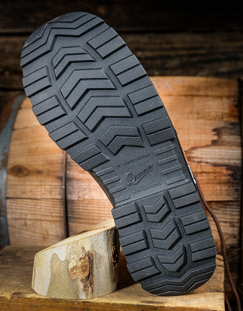 Close-up of a black boot sole with tread pattern on a wooden block against a rustic wooden background