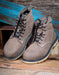 Pair of taupe leather boots with black laces on a wooden surface.