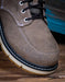 Brown suede shoe with black laces on a wooden surface