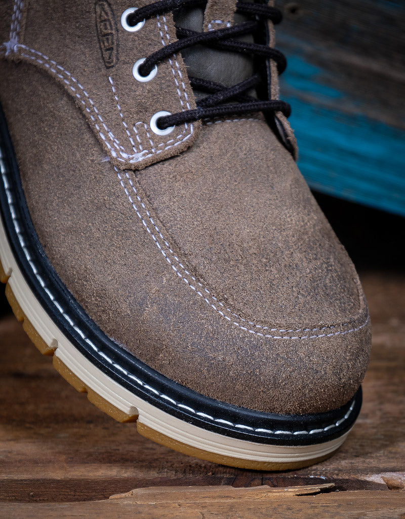 Brown suede shoe with black laces on a wooden surface