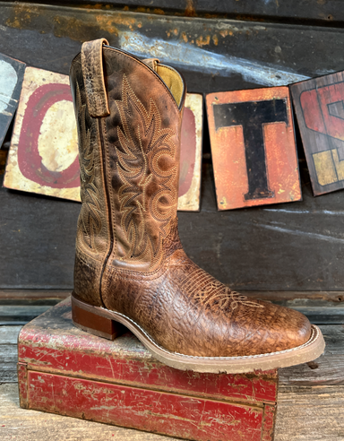 Brown cowboy boot with intricate leatherwork on a rustic background with wooden letters.