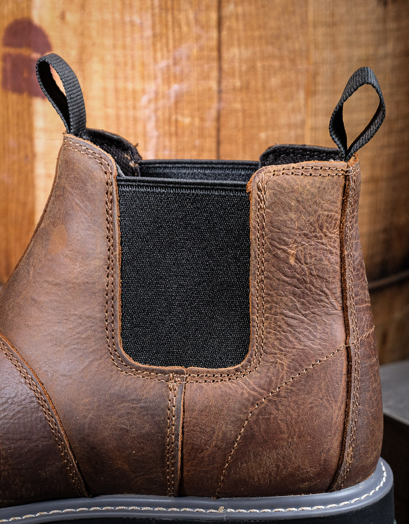 Close-up of a brown leather boot with a black elastic sides on a wooden background