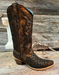 black and bronze cowboy boot with intricate studded detailing on a wooden surface.